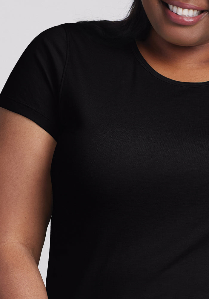 A close-up shows a person smiling in the Woolx Addie Crew Neck - Black, an ultra-soft short-sleeve tee, with only their lower face and upper torso visible.