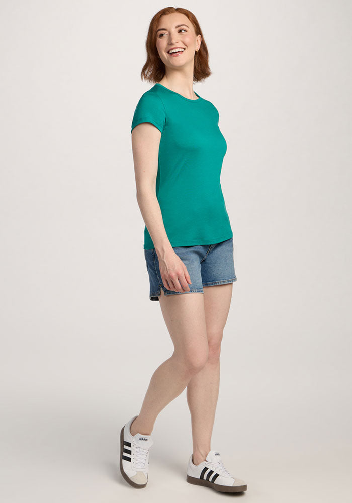 Woman in the Woolx Addie Crew Neck - Cabana Crush smiles, pairing it with denim shorts and sneakers against a light background.