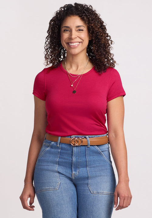 A woman with curly hair smiles, wearing the Woolx Addie Crew Neck in Poppy Spark against a plain background.