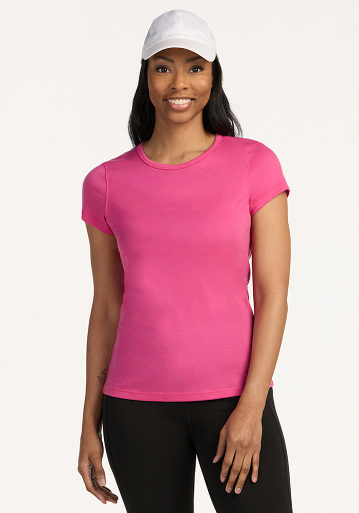 Woman smiling in a Woolx Addie Crew Neck in Raspberry Fizz, paired with a white cap and black pants.