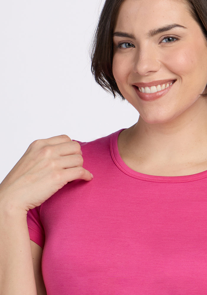 Smiling woman in a Woolx Addie Crew Neck T-shirt in Raspberry Fizz, holding the shirt near her shoulder.