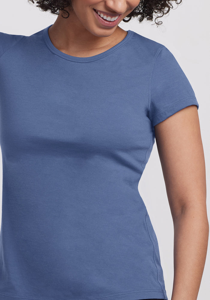 Woman smiling in a fitted blue Woolx Addie Crew Neck (Skyline) shirt against a plain background.