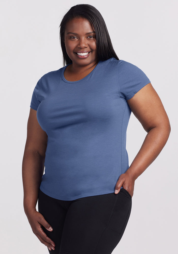 A woman in a Woolx Addie Crew Neck • Final Sale - Skyline shirt and black pants smiles against a plain light background.