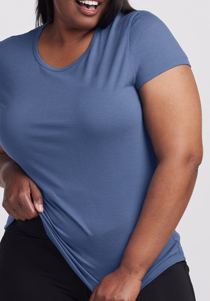 Smiling woman in a Woolx Addie Crew Neck • Final Sale - Skyline, pulling at the hem; only her torso is shown.