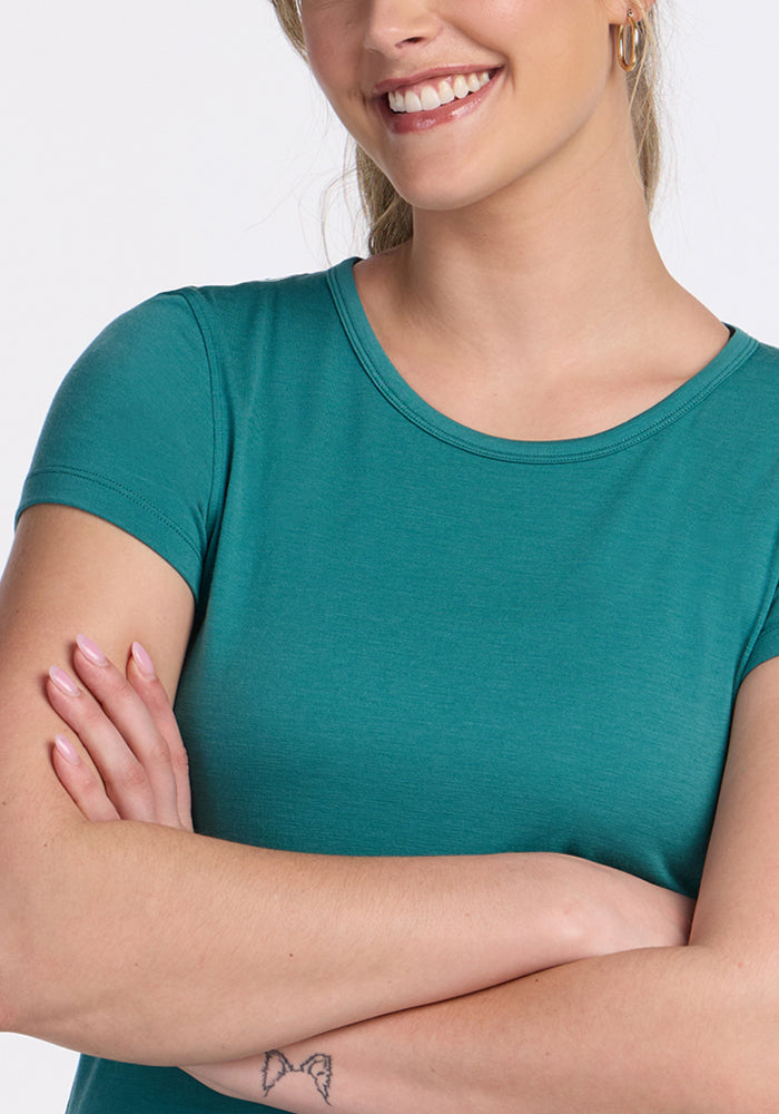 Smiling woman in Woolx Addie Crew Neck Surfside, arms crossed, showing a butterfly tattoo on her forearm.