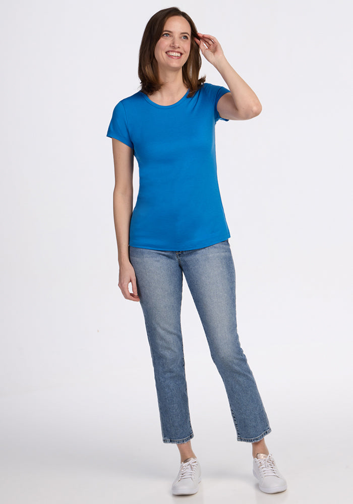 Woman smiling, wearing Woolx Addie Crew Neck in Wave Rider, light blue jeans, and white sneakers on a white background.