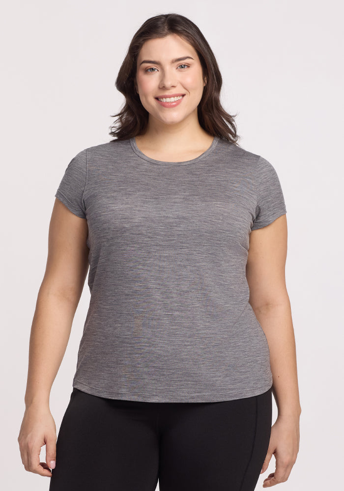 A woman with long dark hair is smiling and wearing the Woolx Addie Crew Neck in Graphite Heather, paired with black pants, standing against a plain light background. | Juliana is 5'10", wearing a size XL