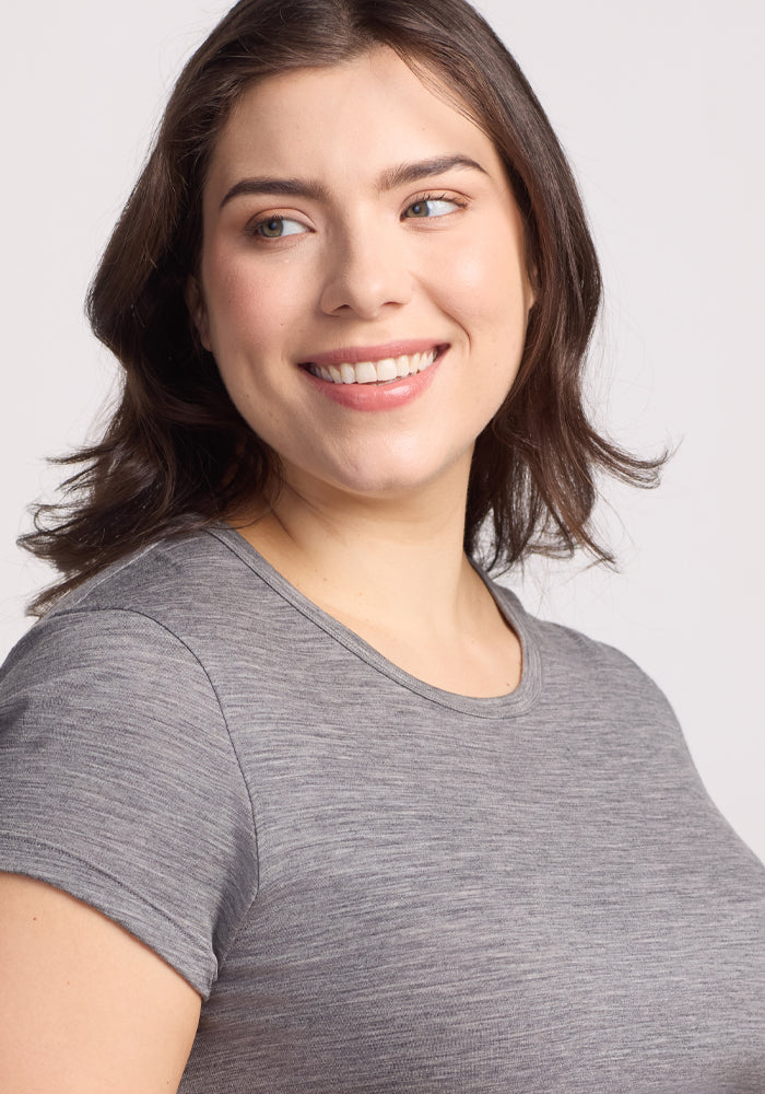 A woman with shoulder-length brown hair smiles while looking to the side, wearing the Woolx Addie Crew Neck in Graphite Heather, against a plain light background.