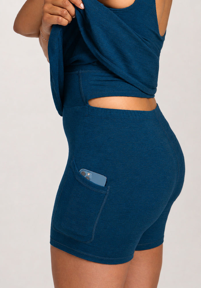 Wearing the Woolx Adrienne Active Dress in Majolica Blue, lifting the hem to show a phone in the built-in shorts pocket.