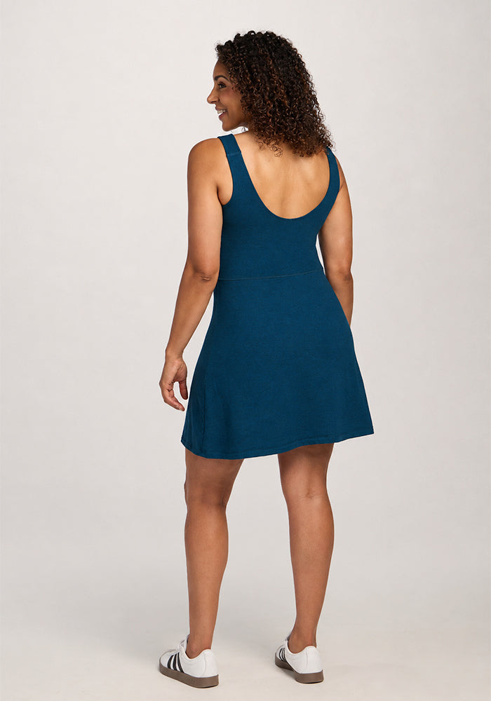 A woman in the Woolx Adrienne Active Dress - Majolica Blue and white sneakers smiles over her shoulder, facing away.