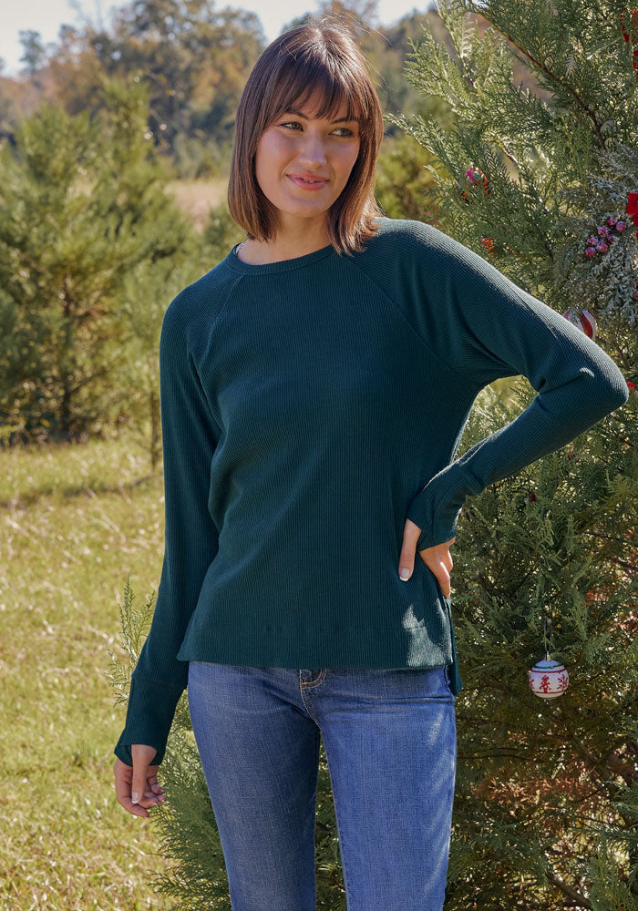 A woman in the Woolx Ainsley Sweater in Deep Timber stands by a Christmas tree, staying cozy and stylish this season.