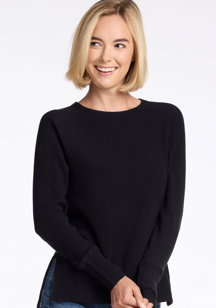 A person with short, blonde hair is smiling while wearing the Woolx Ainsley Sweater in black paired with blue jeans. The background is plain white.  | Georgia is 5'10", wearing a size XS