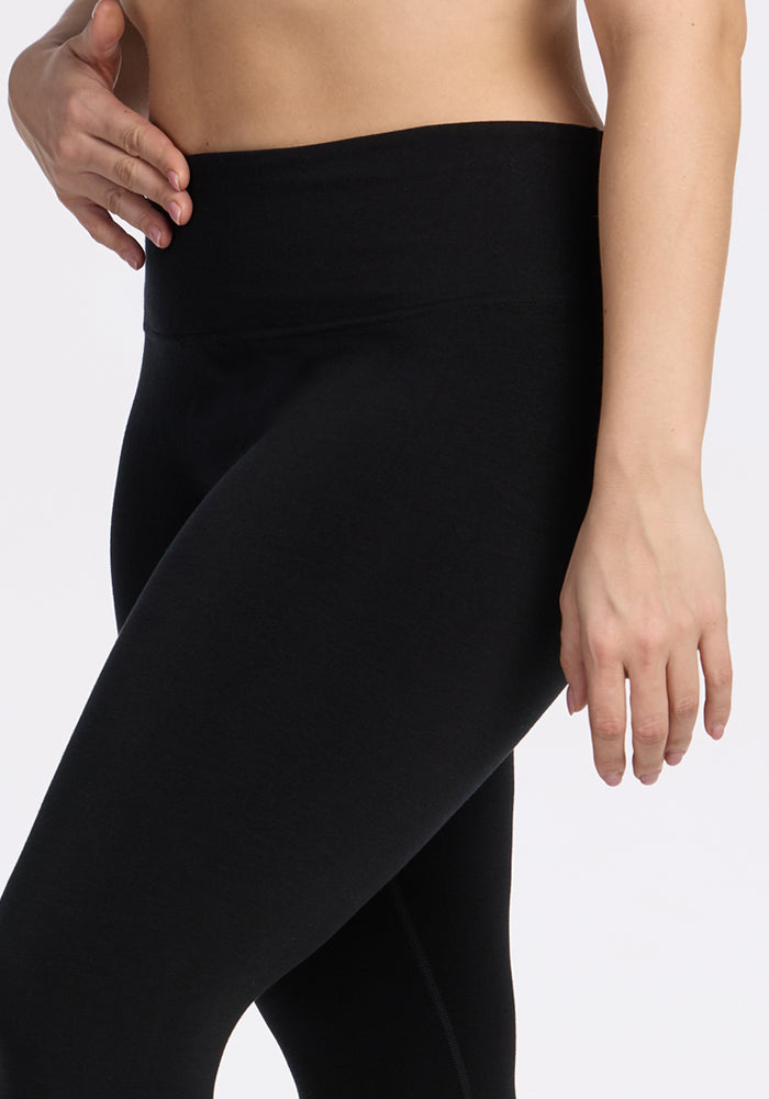 A person wearing Woolx Angela Leggings - Black, shown from mid-torso to upper thigh, with one hand near the hip and the other relaxed by their side against a plain background.