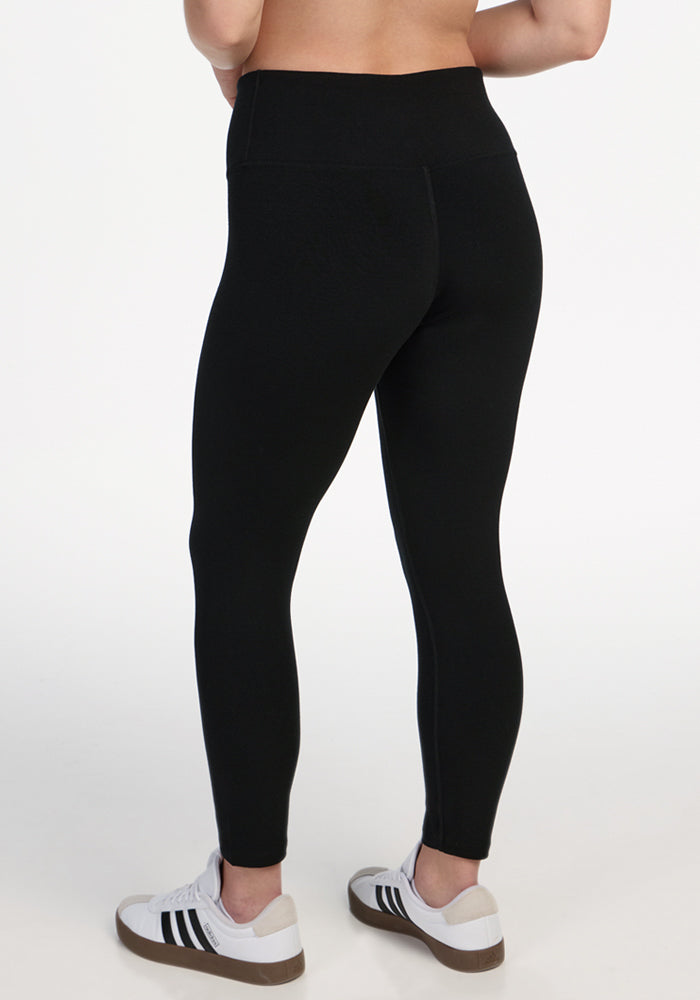 A person is shown from the back waist down, wearing Woolx Angela Leggings - Black and white sneakers with black stripes, standing on a white background.