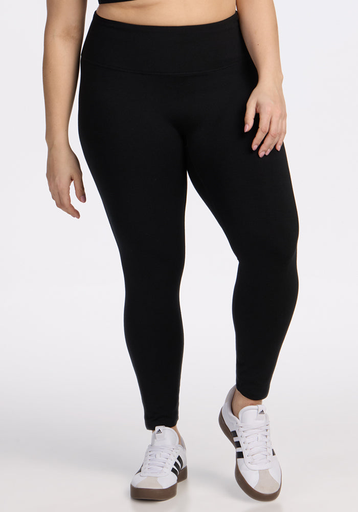 A person wearing Woolx Angela Leggings - Black and white sneakers with black stripes stands against a plain white background. Only the lower half of the body is visible. | Juliana is 5'10", wearing a size XL