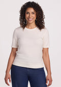 A person with curly hair smiles while standing, wearing the Anna Crew Sweater in Dewdrop Pearl by Woolx and dark jeans. | Kisha is 5’8”, wearing a size M
