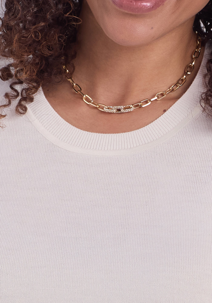 Close-up of a woman wearing the Woolx Anna Crew Sweater in Dewdrop Pearl. Her curly hair peeks through, and she's adorned with a textured gold chain necklace. Only part of her smile and chin are visible.