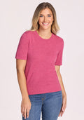 A smiling blonde woman wears the Woolx Anna Crew Sweater in Wild Salmon and blue jeans, standing against a plain light background. | Ariana is 5'11", wearing a size S