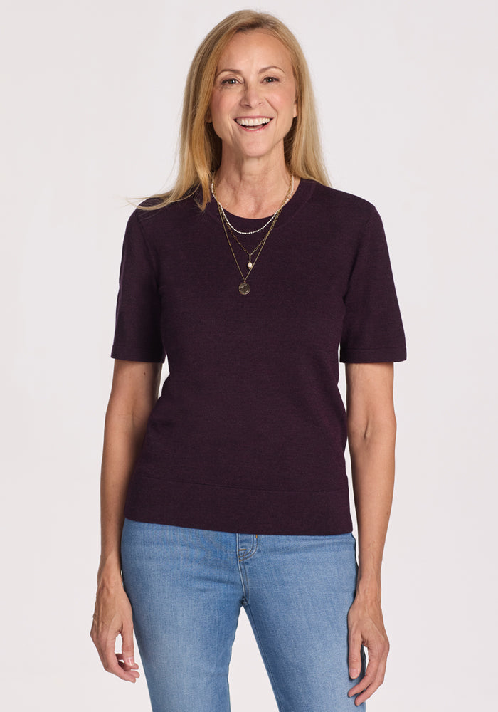 A woman smiles at the camera in the Woolx Anna Crew Sweater in Deep Plum, a cozy merino wool pullover on final sale.