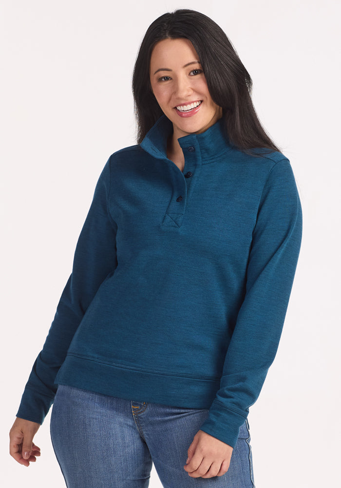 A woman with long dark hair smiles at the camera, wearing the Woolx Annie 3 Button Pullover in Majolica Blue and blue jeans, standing against a plain white background.
