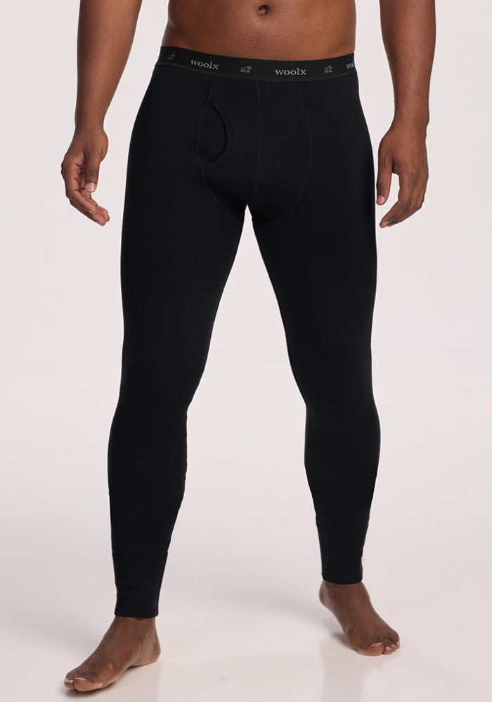 A person wearing black Woolx Arctic Leggings with a visible front fly and branded waistband, standing barefoot against a plain light background. | Trell is 6'2", wearing a size M