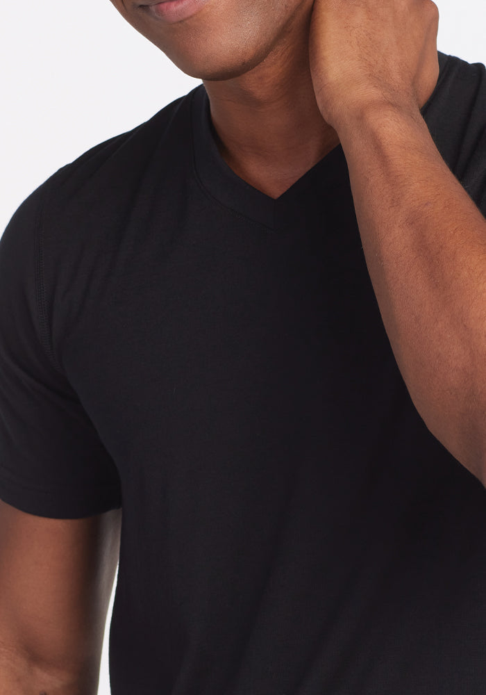 A person wearing the Ashton V Neck - Black by Woolx is touching the side of their neck with one hand. The background is white.