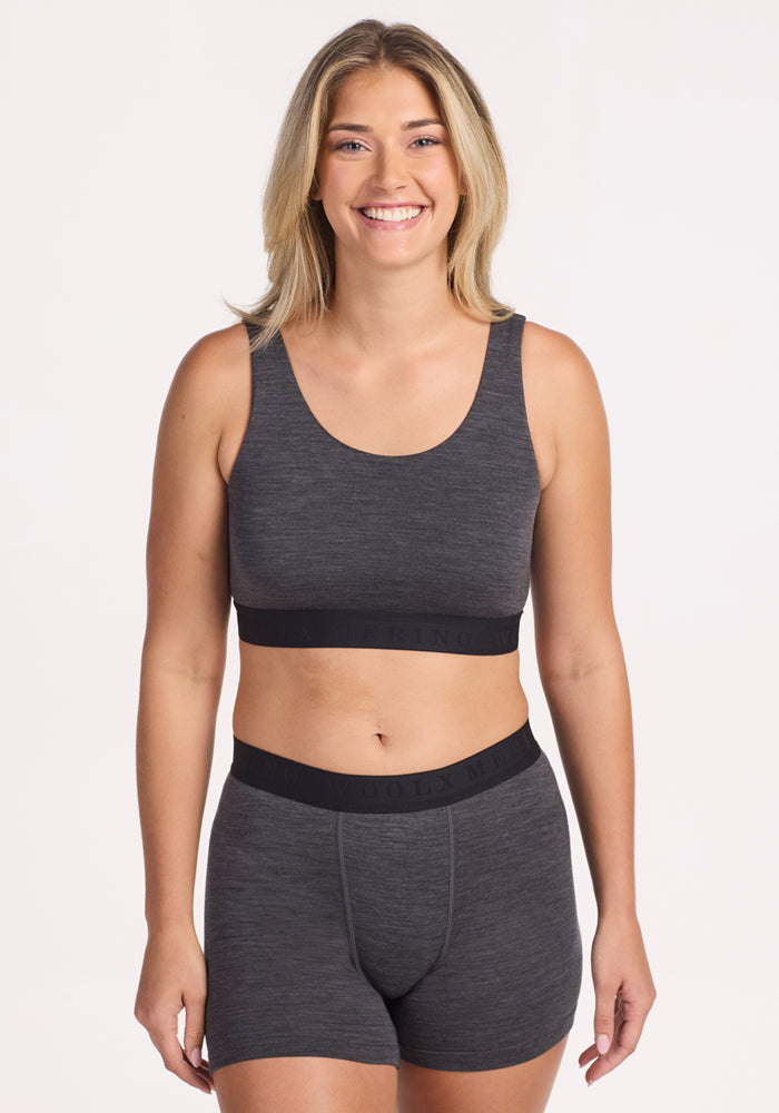 A smiling blonde woman wears the Woolx Aubrey Lounge Bra in Cinder Melange, standing against a plain light background.