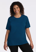 A woman with curly hair smiles while wearing the Woolx Audrey Tee in Majolica Blue and black pants, standing against a plain white background. | Kisha is 5’8”, wearing a size M