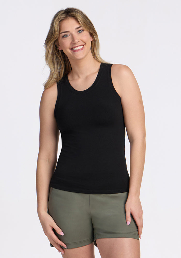 A blonde woman wearing a Woolx Ava Tank Top in black and olive green shorts smiles while standing against a plain white background. | Ariana is 5'11", wearing a size S