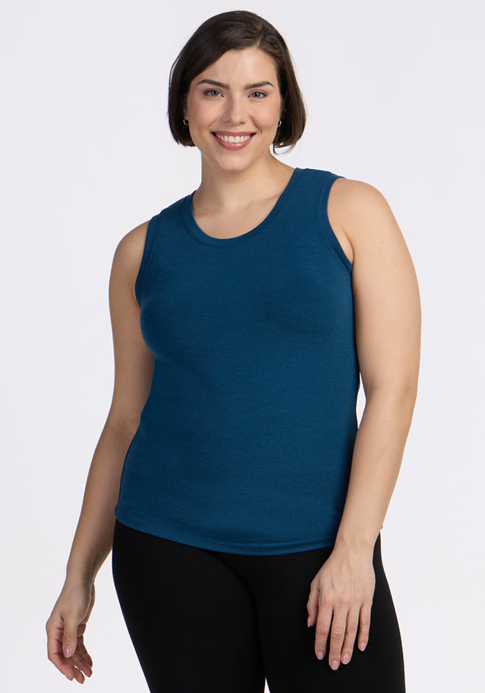 A woman with short brown hair smiles while wearing the Woolx Ava Tank Top in Majolica Blue and black pants, standing against a plain white background. | Juliana is 5'10", wearing a size XL