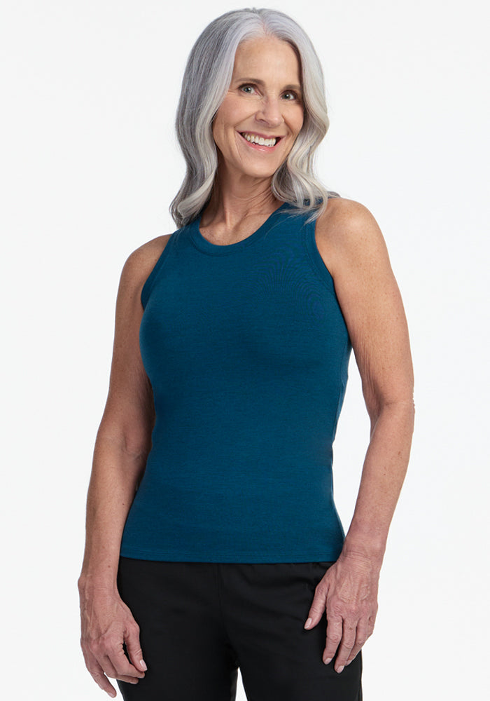 Smiling older woman with long gray hair wears the Woolx Ava Tank Top in Majolica Blue and black pants, standing against a plain white background. | Tam is 5’8.5”, wearing a size S