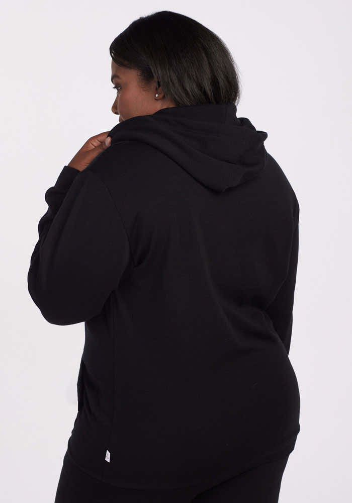 A person with dark hair models the Woolx Avery Hoodie in black, made from recycled polyester, shown from the back and looking over their left shoulder against a plain light background. Final Sale Deals!.