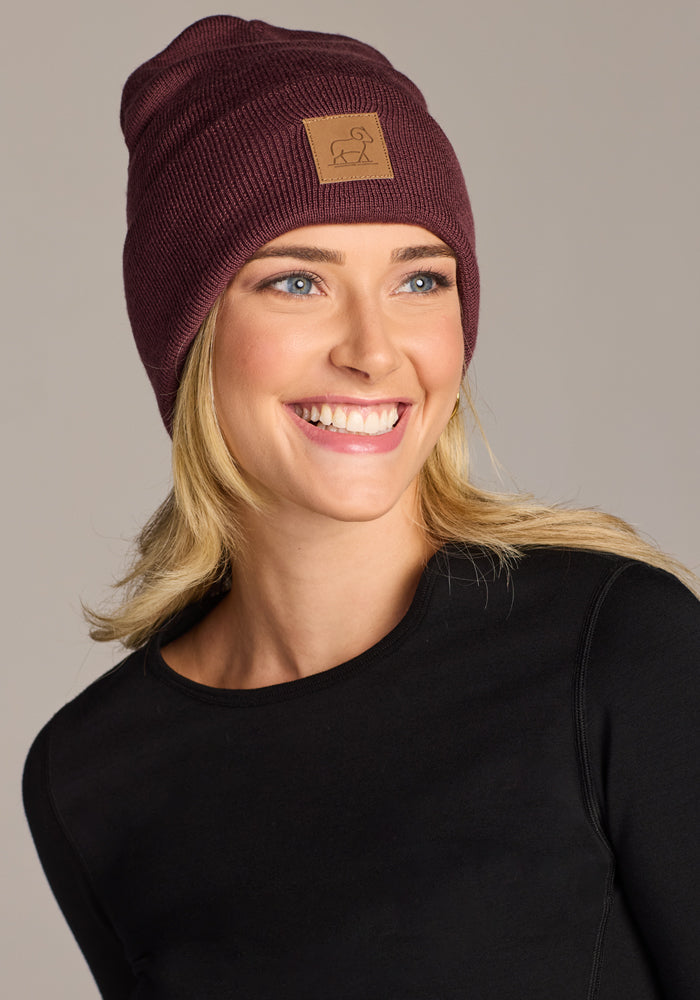 A woman smiles wearing the Woolx Baylor Beanie in Grape Harvest, crafted from cozy Australian merino wool.
