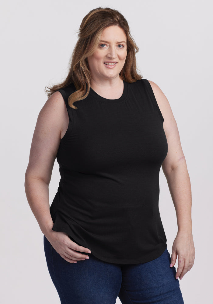 A person with long hair in a classic Bella Tunic Top - Black by Woolx and blue jeans smiles against a plain white background, truly embodying a timeless summer staple. | Cambre is 5'11", wearing a size XL