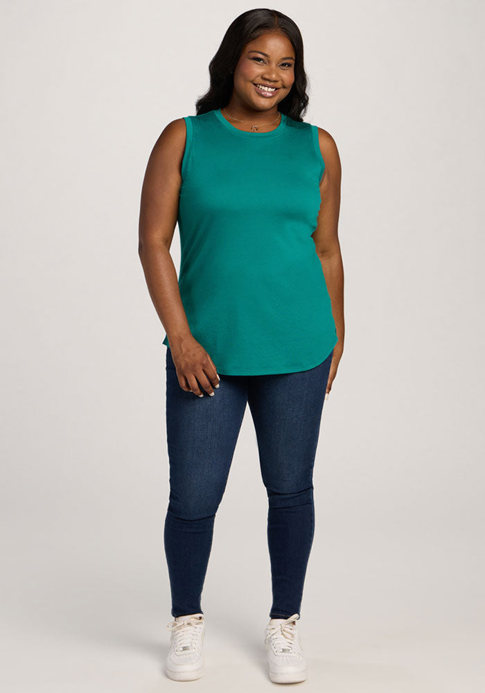 Smiling woman in Woolx Bella Tunic Top - Cabana Crush and dark jeans, wearing white sneakers against a plain background.