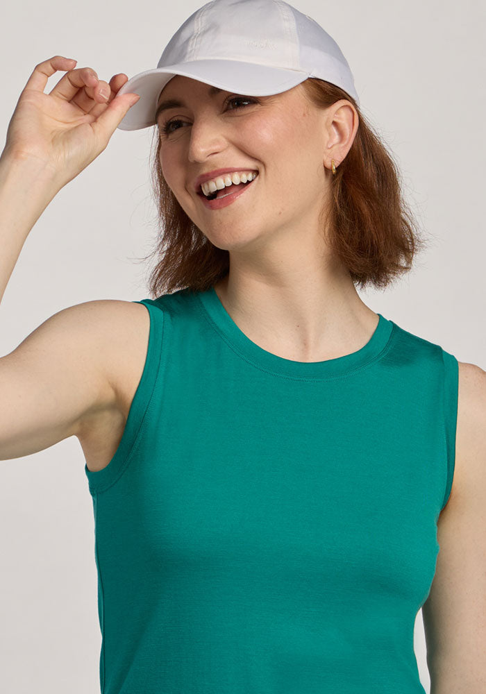 Woman smiling in a Woolx Bella Tunic Top - Cabana Crush and white cap, touching her hat against a light background.