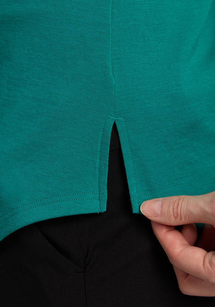 Close-up of a hand holding the hem of the Woolx Bella Tunic Top - Cabana Crush over black pants.