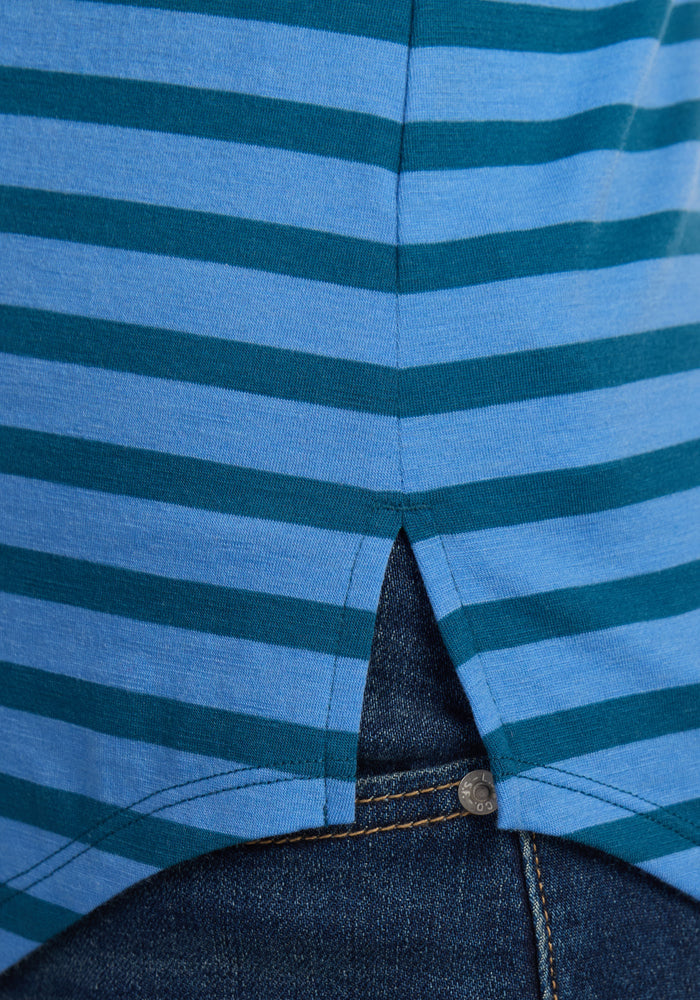 Close-up of the Woolx Bella Tunic Top - Coastal Stripe, a blue and teal striped women’s summer tank with a small side slit, worn untucked over blue denim jeans. Showcases the top’s relaxed fit and visible stitching on the jeans.