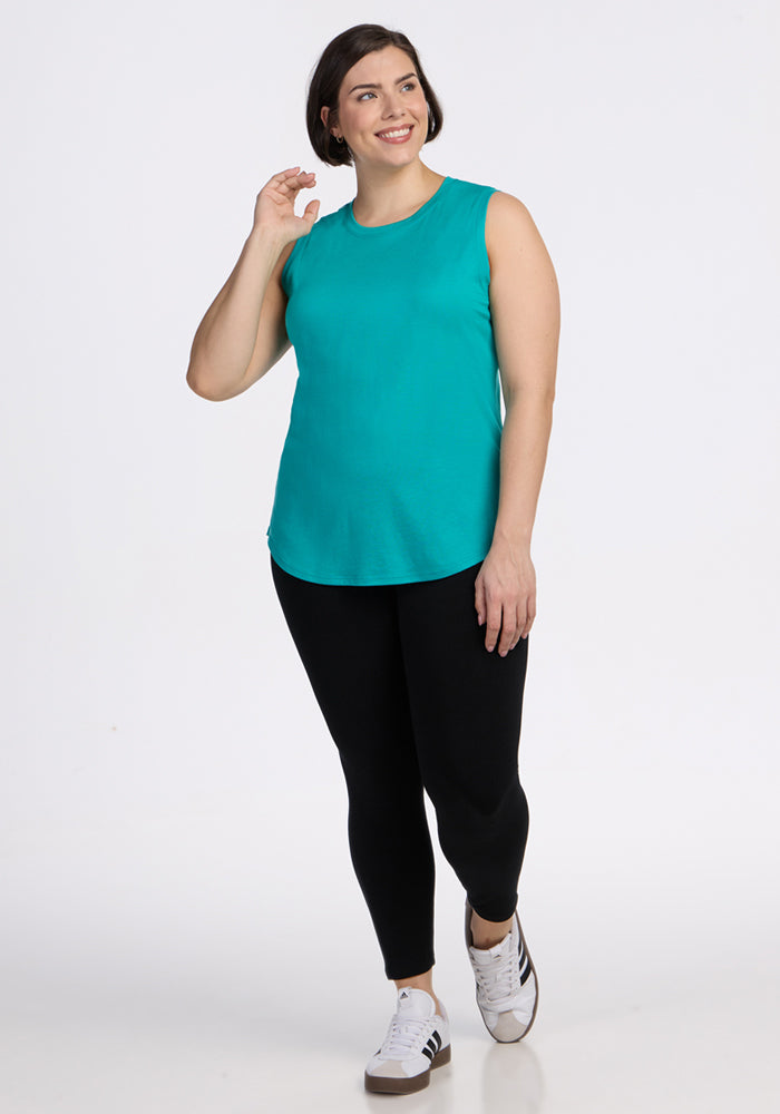 Woman smiling in the Woolx Bella Tunic Top - Cool Jade, black leggings, and white sneakers against a white background.