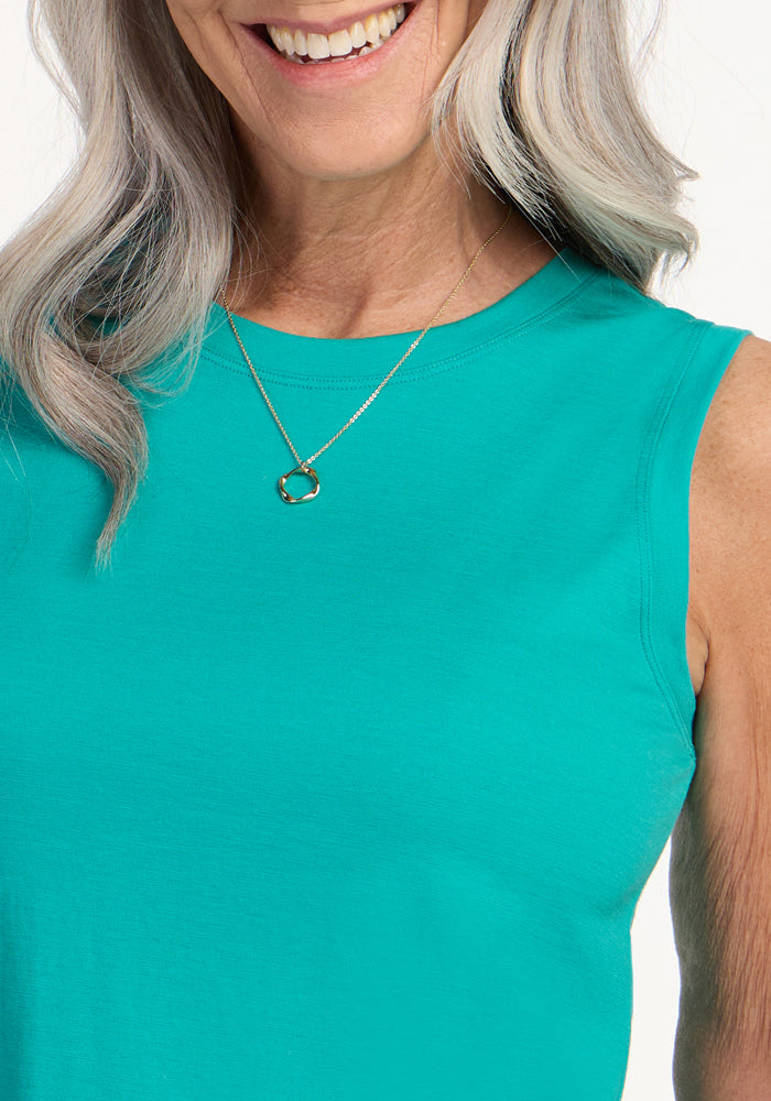 Smiling woman with long gray hair wears the Woolx Bella Tunic Top in Cool Jade and a gold necklace on a white background.