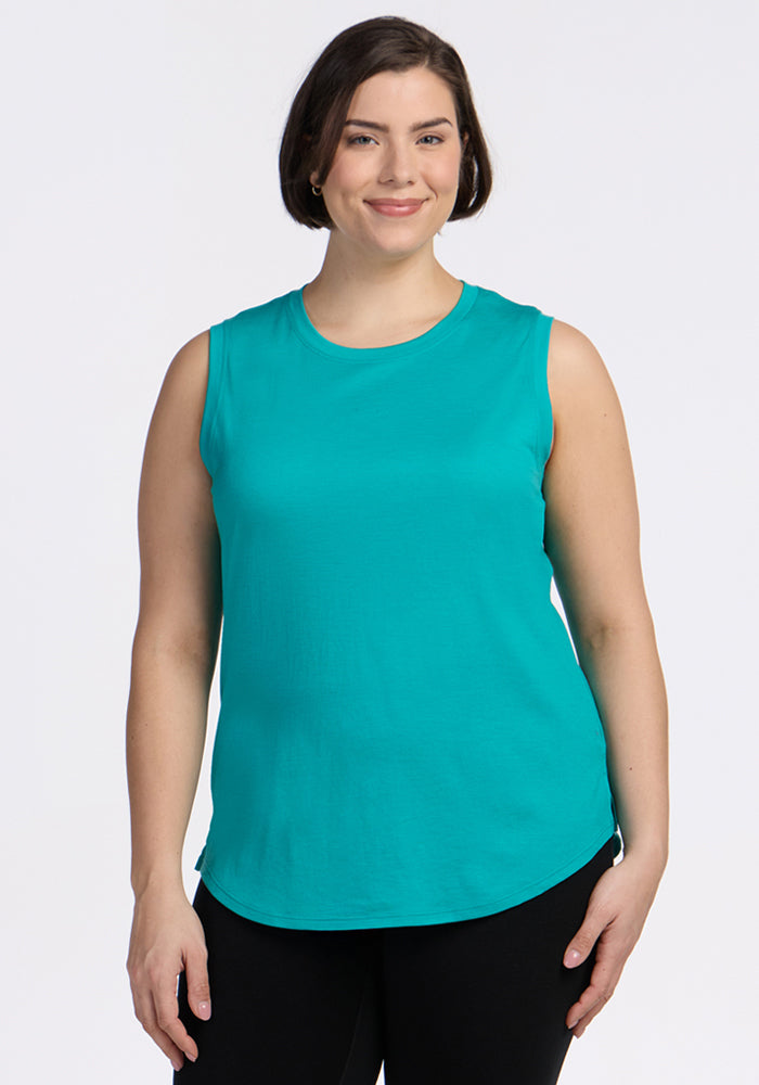 Smiling woman in a Woolx Bella Tunic Top in Cool Jade and black pants, posed against a plain white background.