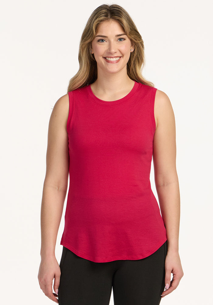 Smiling woman in Woolx Bella Tunic Top in Poppy Spark and black pants stands against a plain white background.