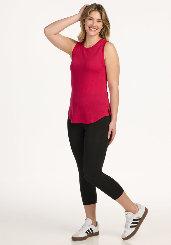 Woman smiling in a Woolx Bella Tunic Top in Poppy Spark, black leggings, and white sneakers against a white background.