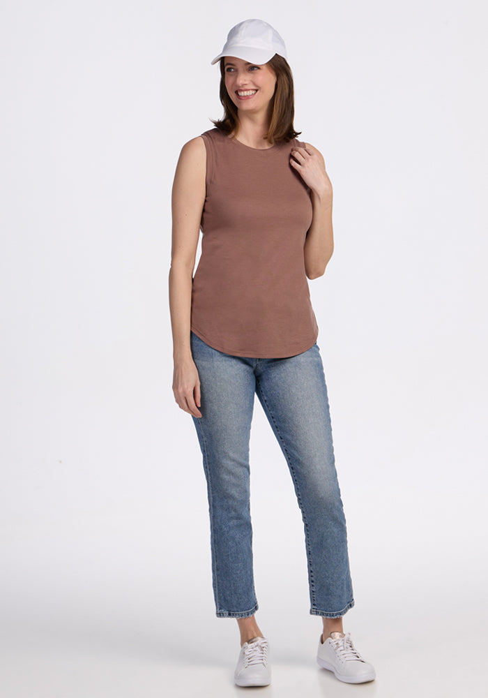 Woman smiling, wearing Woolx Bella Tunic Top in Sienna Kiss with blue jeans, white cap, and white sneakers.