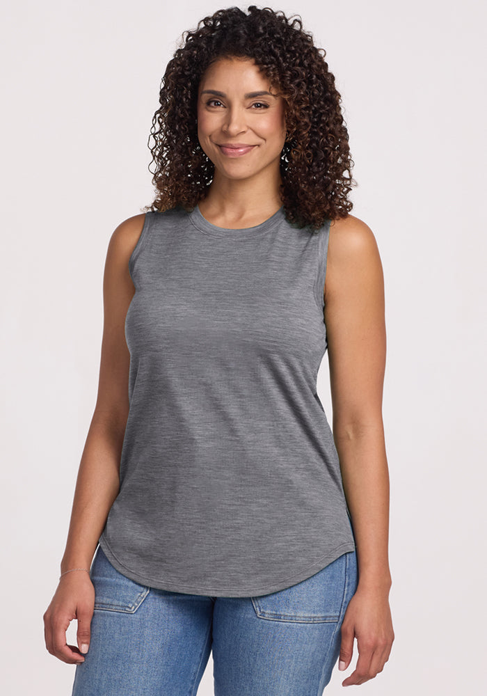 A woman with curly hair, smiling, wears the Woolx Bella Tunic Top in Graphite Heather and blue jeans against a plain light background. | Kisha is 5’8”, wearing a size M
