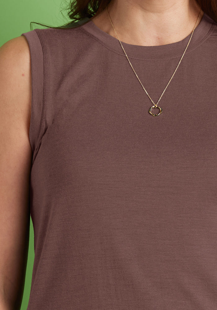 A woman in a Woolx Bella Tunic Top in Peppercorn with a gold necklace stands before a green background.