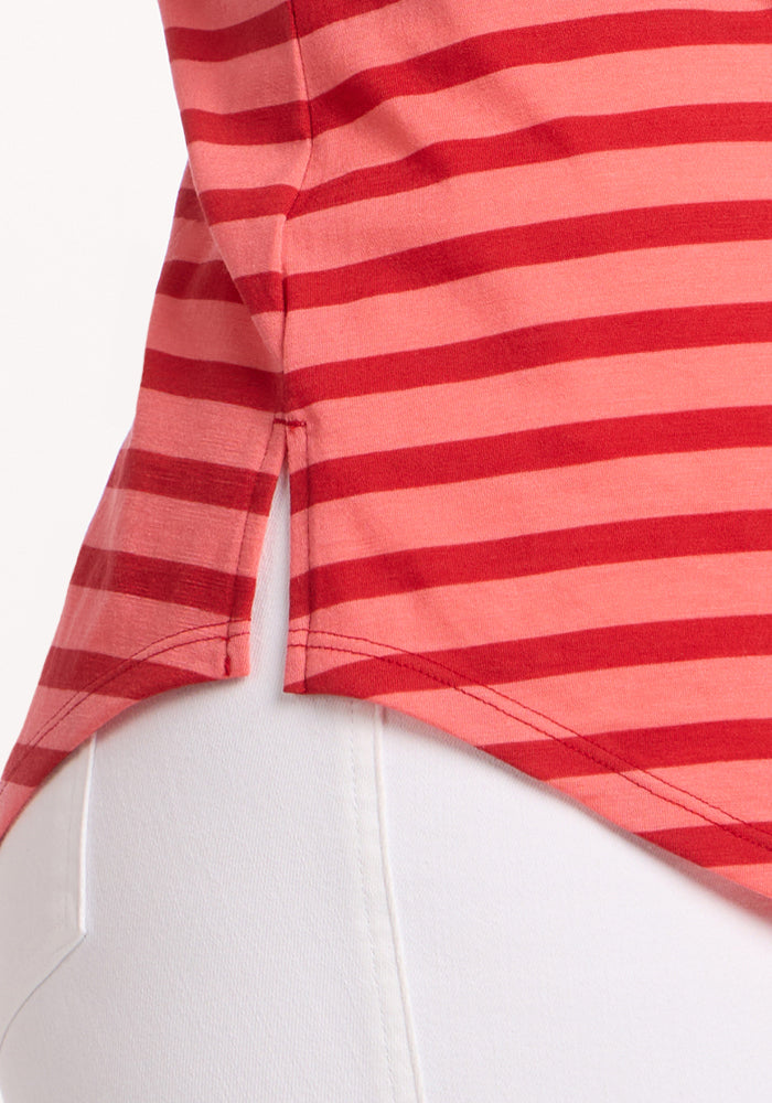 Close-up of the Woolx Bella Tunic Top in Wildberry Stripe, a lightweight merino summer shirt with red and pink stripes, side slit at the hem, and detailed side seam, shown worn over white pants.