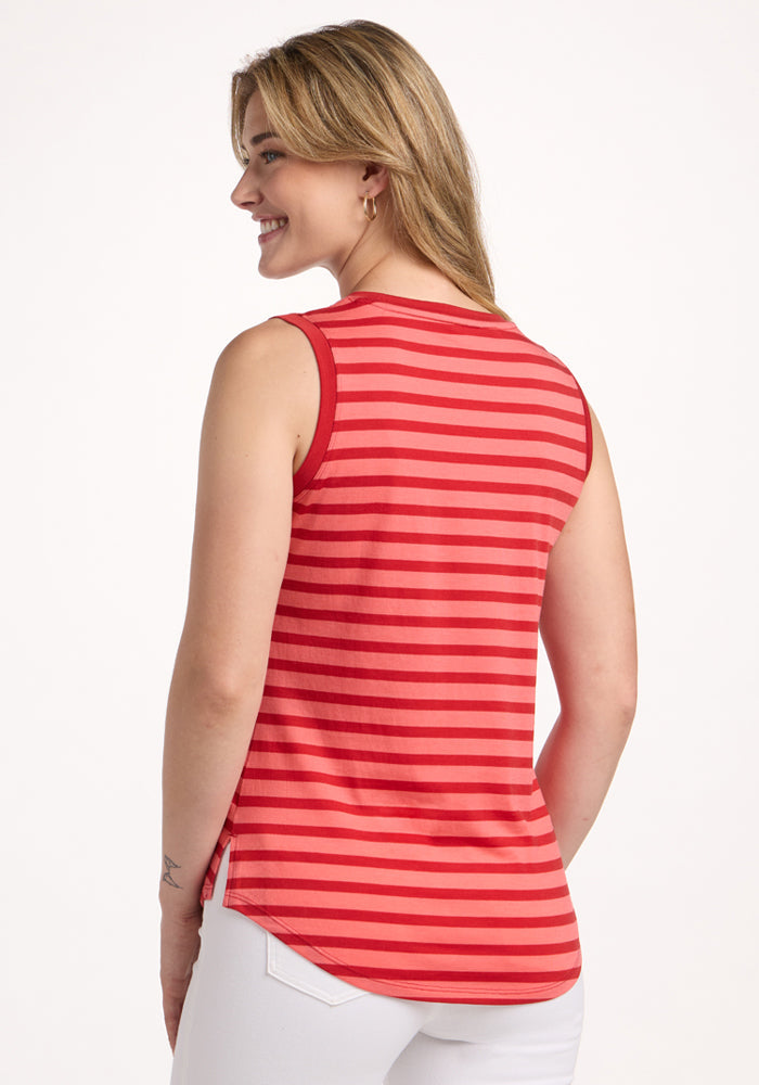 A woman with light brown hair smiles and looks to the side, wearing the Woolx Bella Tunic Top in Wildberry Stripe and white pants, shown from the back against a plain white background.