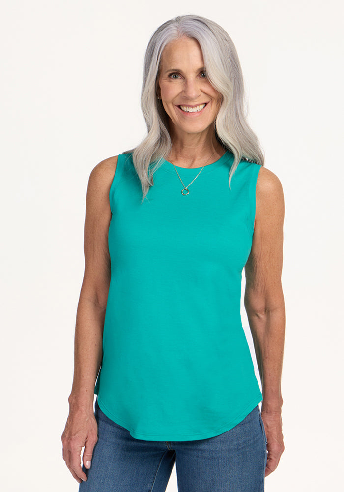 Smiling woman in a Woolx Bella Tunic Top • Final Sale - Cool Jade and blue jeans, against a plain background.
