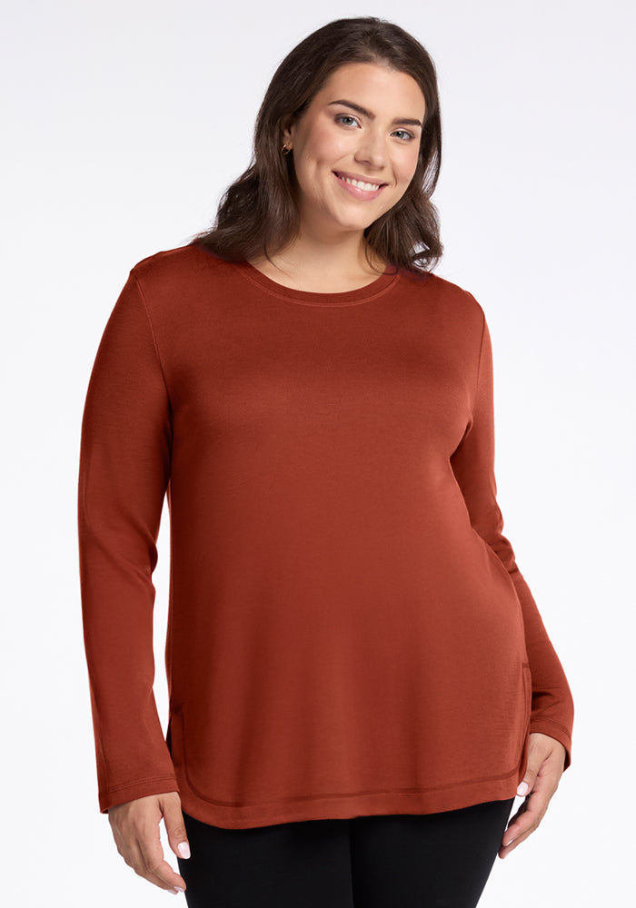 A woman with long brown hair smiles while wearing the Woolx Blair Tunic in Maple Leaf (final sale), paired with black pants, standing against a plain white background.